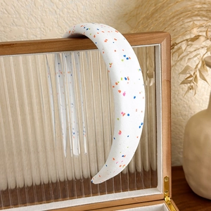 Détail du serre-tête en éponge avec des points de peinture colorés sur tissu blanc
