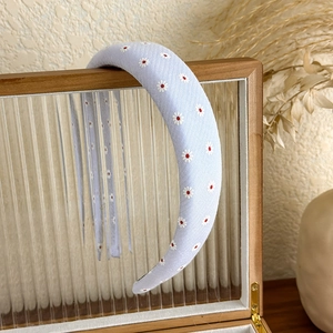 Close-up of light blue padded headband featuring white daisy embroidery on textured fabric