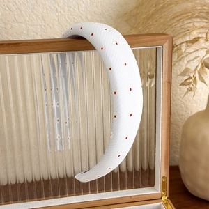 Détail d'un serre-tête blanc épais orné de motifs floraux rouges et jaunes fins