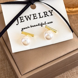 Detailed macro view of minimalist gold bar and white pearl earrings on a premium jewelry box