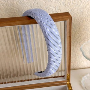 Gros plan du serre-tête en tissu rayé bleu clair avec perles argentées sur boîte