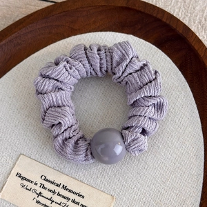 Détail d'un chouchou en tissu plissé lilas avec un grand ornement de perle brillante