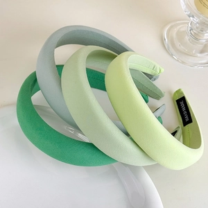 Three-pack of green sponge headbands in matte fabric with handmade label in a ceramic plate