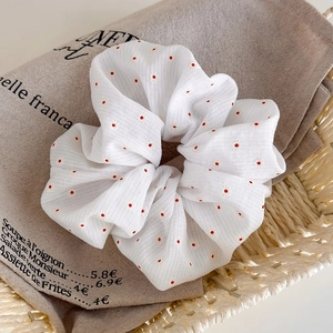 Détail d'un chouchou blanc à pois rouges posé sur un sac en lin de style français
