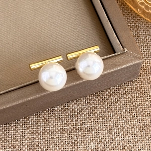 Detail view of elegant pearl stud earrings featuring gold horizontal bars on a brown tray