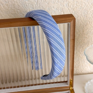 Détail d'un serre-tête en tissu rayé bleu avec strass sur boîte de présentation