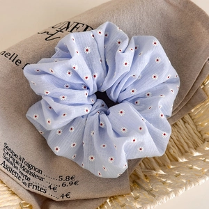 Détail d'un chouchou bleu clair avec broderie de marguerites sur texture de lin