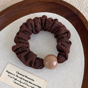 Gros plan d'un chouchou en tissu plissé marron foncé avec une perle en résine vintage