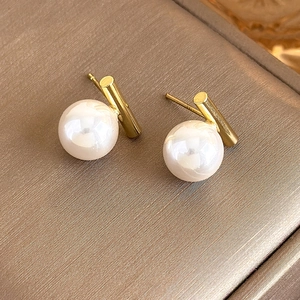 Macro shot of minimalist pearl earrings with gold cylindrical posts on a silk surface