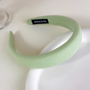 Detail view of a padded light green fabric headband with a handmade textile label
