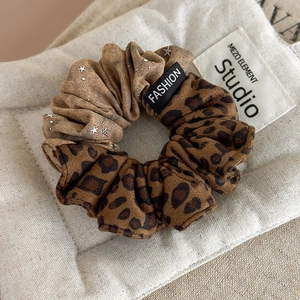 Leopard and star print scrunchie with fashion label on a beige quilted background