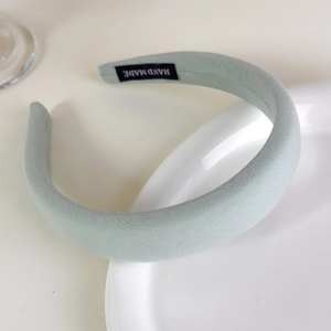 Close-up of sage green sponge headband with Hand Made label on a white ceramic tray