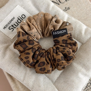 Close-up of leopard and star print scrunchie with fashion label on linen background