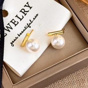 Detailed macro view of minimalist pearl stud earrings with gold bars in a jewelry box