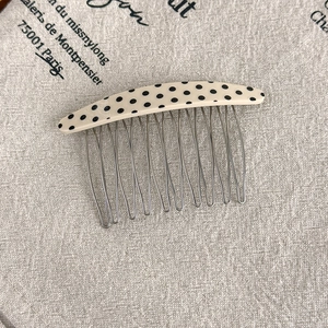 Detail of vintage polka dot acetate comb showing 10-tooth metal prongs on linen