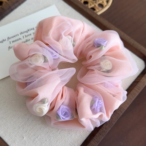 Détail d'un chouchou en organza rose avec roses en tissu 3D sur plateau en bois