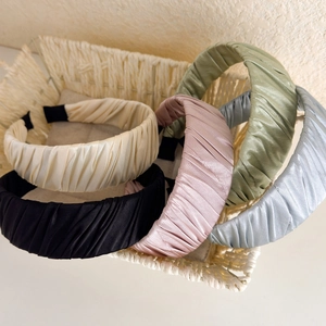 Close-up of five pleated satin headbands in neutral colors inside a white woven basket