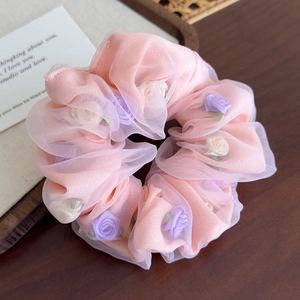 Détail d'un chouchou en organza rose avec des roses en tissu violet et crème