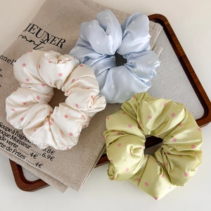 Vue détaillée de trois chouchous en satin à pois crème, bleu et vert sur un plateau en bois