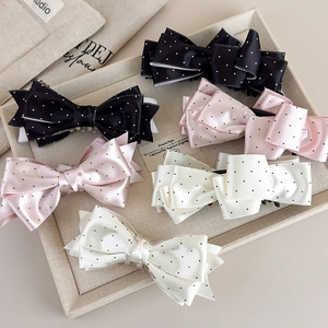 Tre eleganti fermagli per capelli in raso a pois neri, rosa e crema sul vassoio