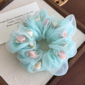 Détail d'un chouchou en organza bleu clair avec de délicates roses en tissu rose et blanc