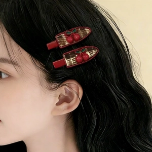 Pair of red cherry hair clips with gold leaves on model's dark curly hair