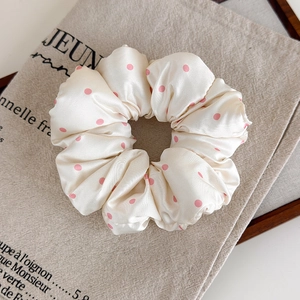 Vue détaillée d'un chouchou en satin crème à pois roses sur un fond de sac en lin naturel