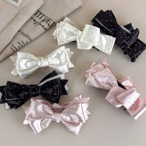 Dettaglio dei fermagli in raso a pois nei colori panna, nero e rosa con fiocchi a strati