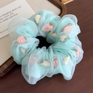 Gros plan sur un chouchou en organza bleu clair orné de petites roses en tissu rose et blanc