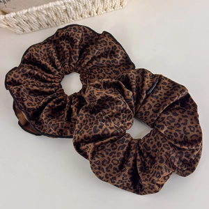 Detail of two leopard print velvet scrunchies with black stitched edges on white background