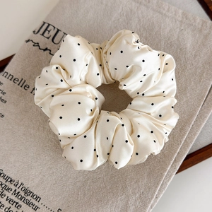 Détail d'un chouchou en satin à pois rembourré posé sur un tissu en lin vintage