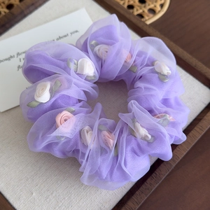 Détail d'un chouchou en organza violet avec des roses en tissu et de délicates feuilles vertes