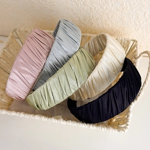 Close-up of pleated satin headbands in five soft colors displayed in a woven basket