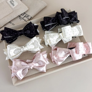 Dettaglio dei fermagli per capelli in raso a pois nei colori nero, crema e rosa