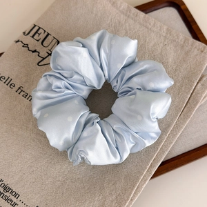 Détails de la texture du chouchou en satin bleu clair à pois blancs sur tissu beige