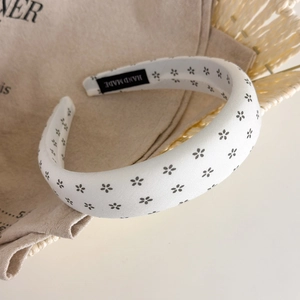 Close-up of white sponge headband with black floral pattern and handmade cloth label