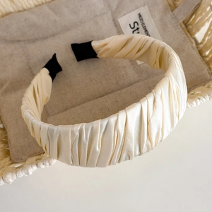 Detail of pleated cream satin headband with elegant texture and black non-slip ends