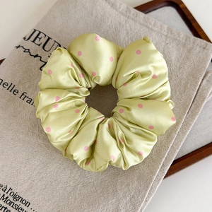 Détail d'un chouchou en satin vert clair à pois roses avec une texture plissée douce
