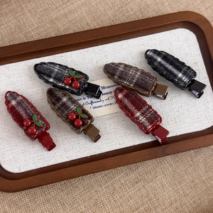 Detailed view of red cherry hair clips with plaid fabric texture in wooden display tray