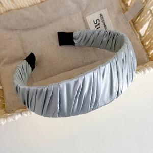 Detail view of light blue satin headband with elegant pleated texture and black tips