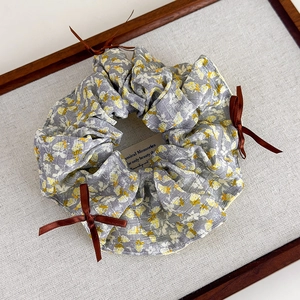 Details des grauen Blumen-Scrunchies mit gelben Mustern und braunen Satinschleifen