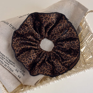 Close-up of leopard print velvet hair scrunchie with refined black edging on linen