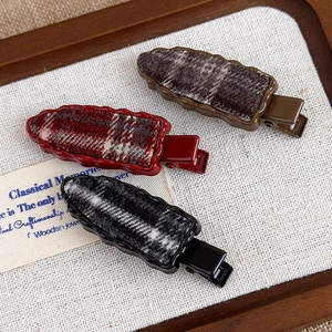 Detail of red and black plaid textured hair clips displayed on vintage linen fabric