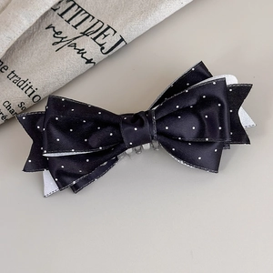 Dettaglio di un fermaglio per capelli in raso nero a pois su sfondo di lino minimalista