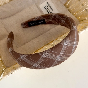 Detailed close-up of a brown plaid headband with a woven HAND MADE interior label