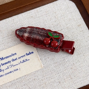 Detail of red cherry hair clip with dark red frame and checkered fabric on beige canvas