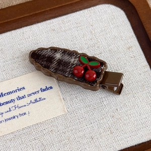 Close-up of a vintage cherry hair clip with red fruit and green leaves on dark plaid fabric