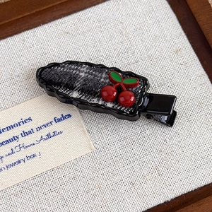 Detail of red cherry hair clip with black and white tweed fabric on scalloped edge