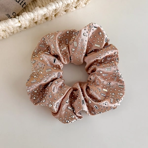 Detailansicht eines roségoldenen Satin-Haargummis mit funkelnden weißen Strasssteinen