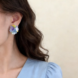 Boucles d'oreilles fleurs d'hortensia colorées sur un modèle avec une tenue bleu pastel